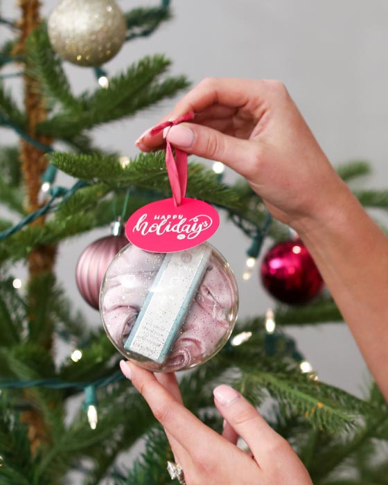 Woman holding Neora's hottest holiday must-have, the All Eyes on You Set, which includes Age IQ® Eye Serum, Eye-V™ Moisture Boost Hydrogel Patches and FREE Eye Mask next to a Christmas tree.